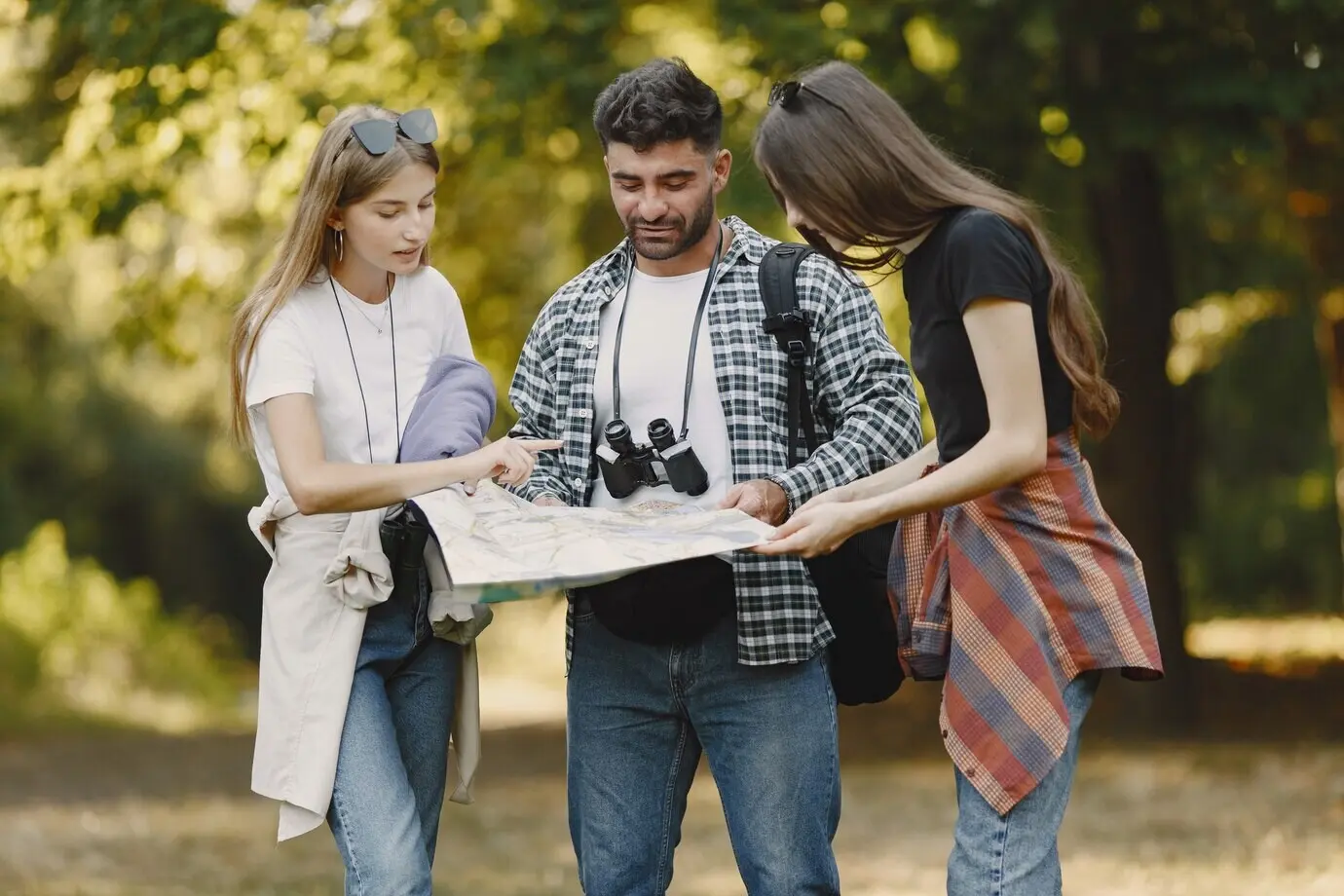 Concept of adventure, hiking, and people. A group of smiling friends in a forest. A man with binoculars.